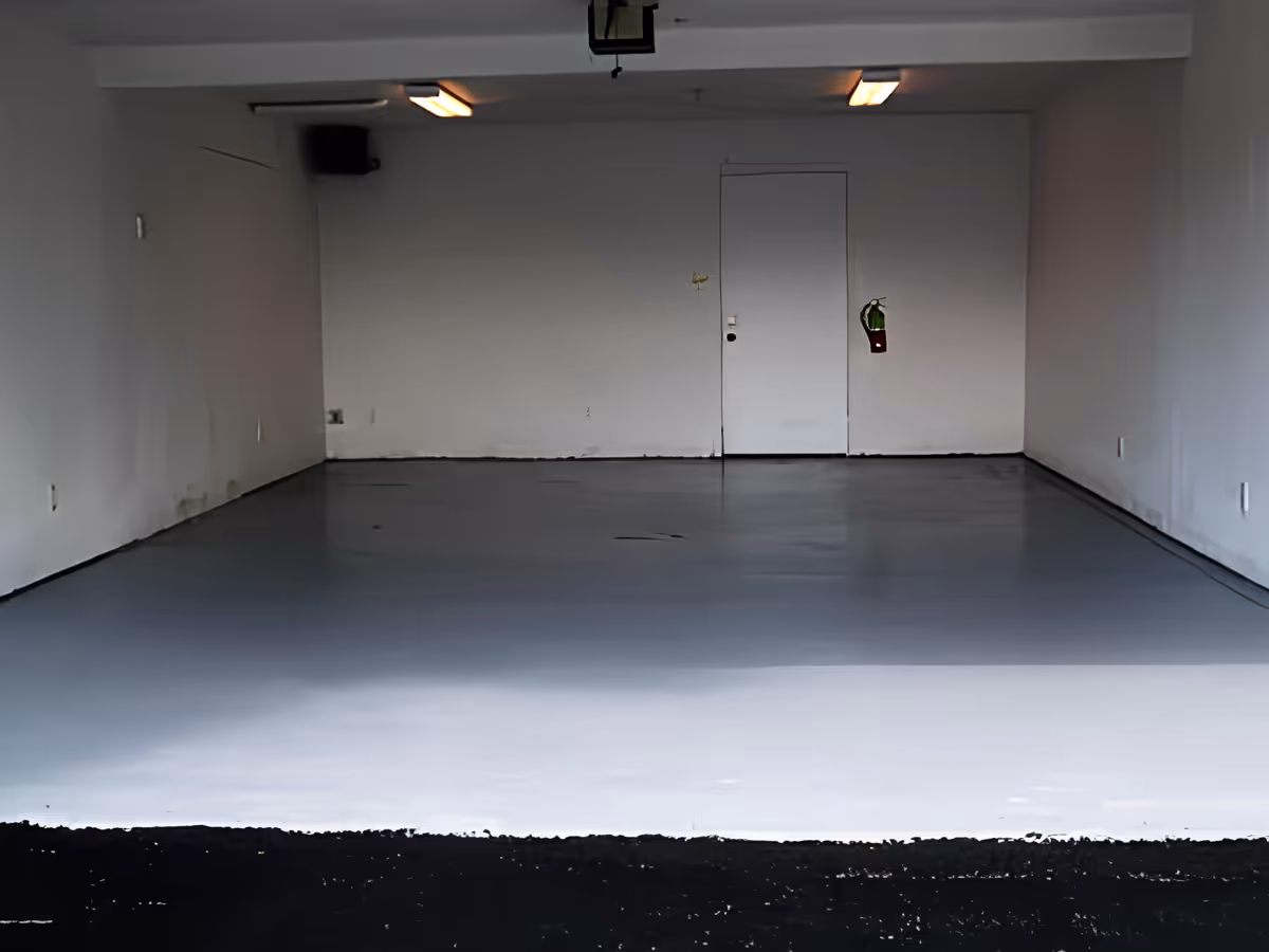 Empty indoor garage-like room with a smooth gray floor, white walls, a central door and a wall-mounted fire extinguisher.