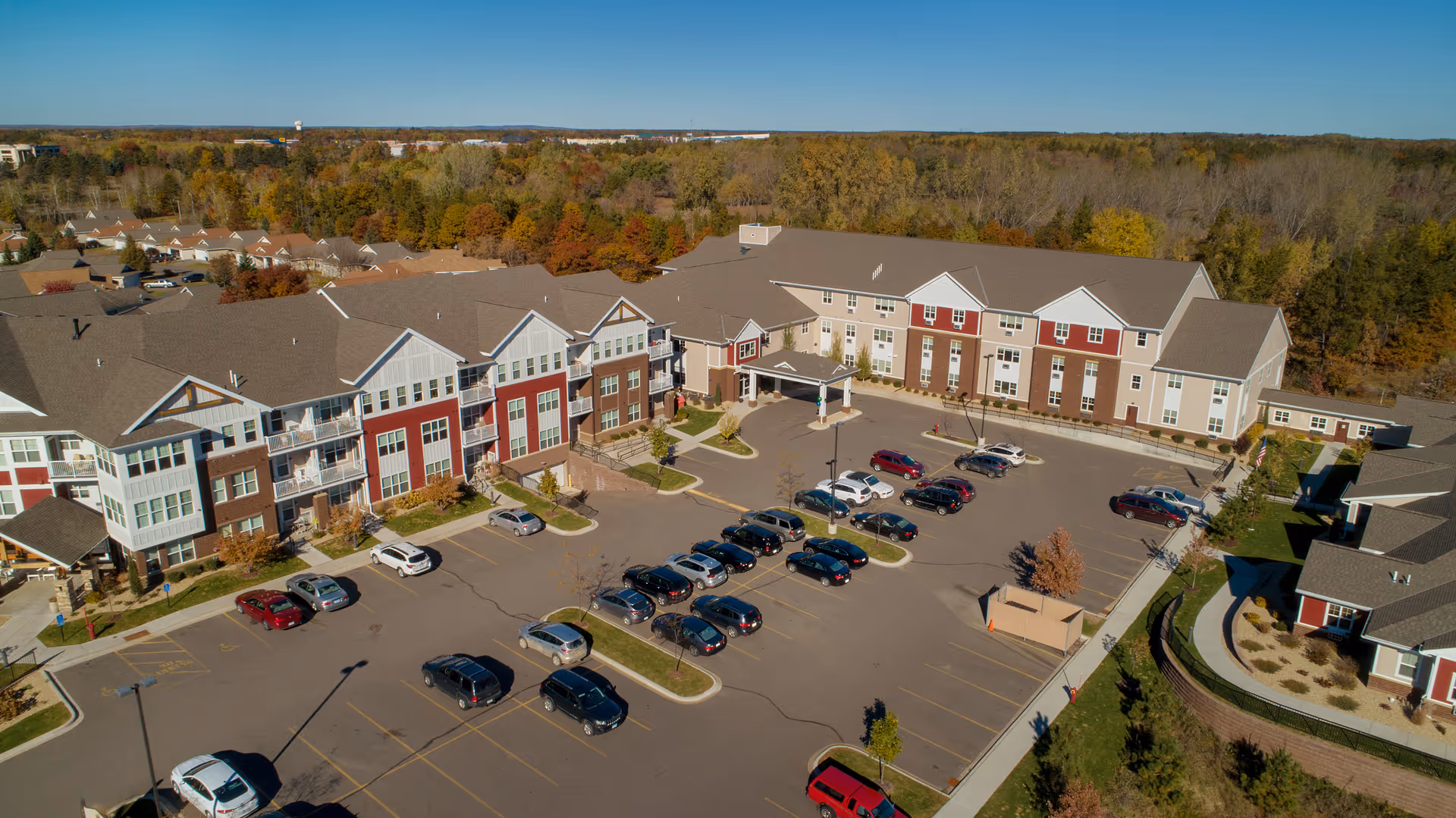Aerial view of the Northern Lakes Senior Living complex showing multi-story residential buildings, entrance drive, and a parking lot surrounded by trees.