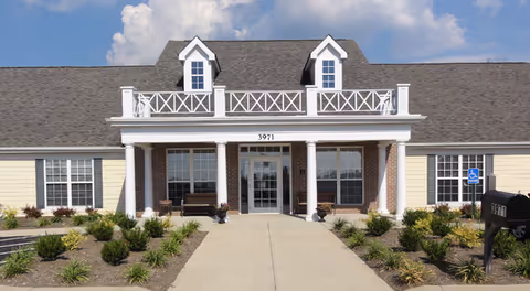 Front entrance of a single-story senior living building with a covered porch supported by white columns, walkway, landscaping, and the address number 3971.
