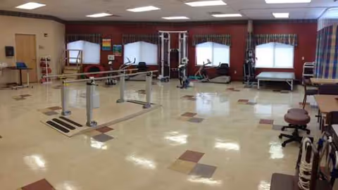 Rehabilitation gym in Heartland Health Care Center-Briarwood with parallel bars and equipment.
