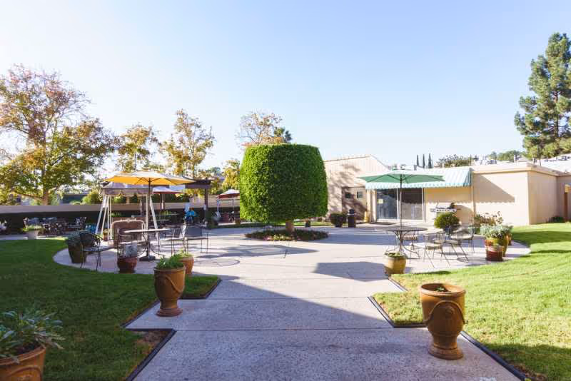 Outdoor courtyard at Country Manor La Mesa Healthcare Center with shaded seating and potted plants.
