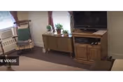 Small living room with a TV on a wooden cabinet, a sideboard with potted plants, and a rocking chair by the window.