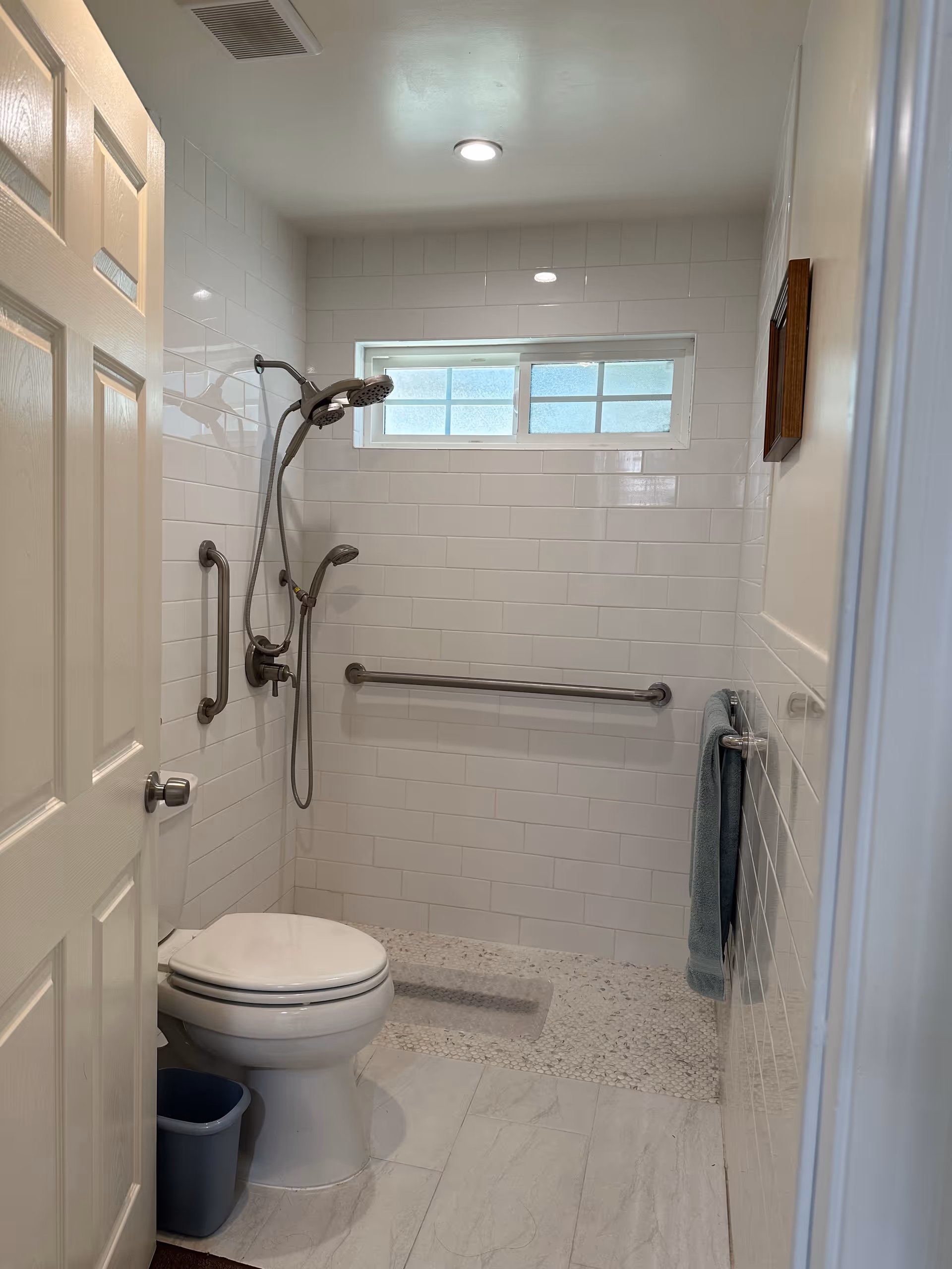 Accessible bathroom with a toilet, handheld shower, multiple grab bars and tiled walls and floor.