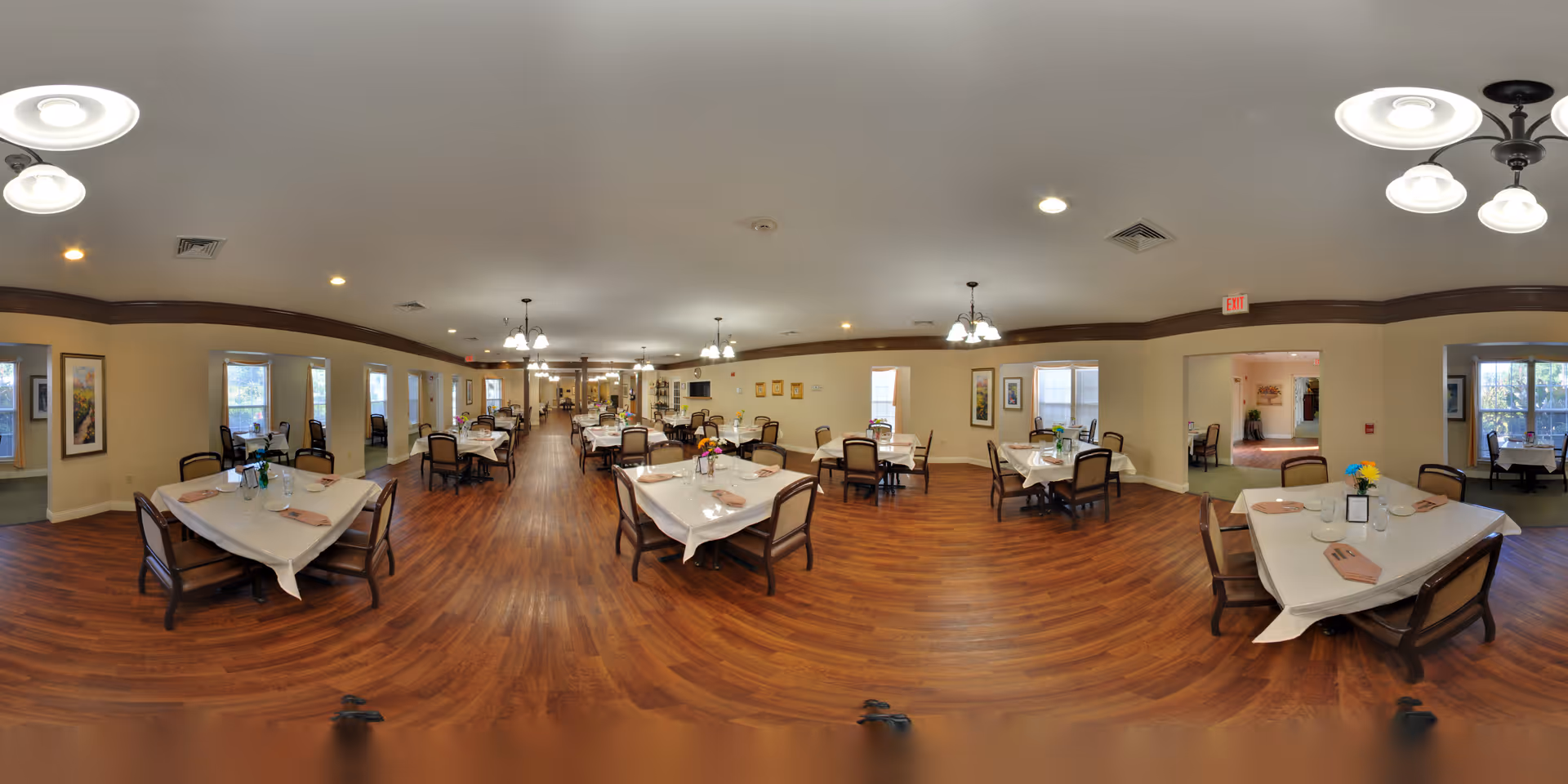 Spacious communal dining room with multiple tables set for meals and wood floors.