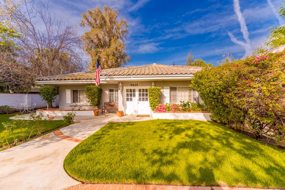 Front exterior of a single-story home with a tiled roof, manicured lawn, American flag, and a walkway leading to double front doors.