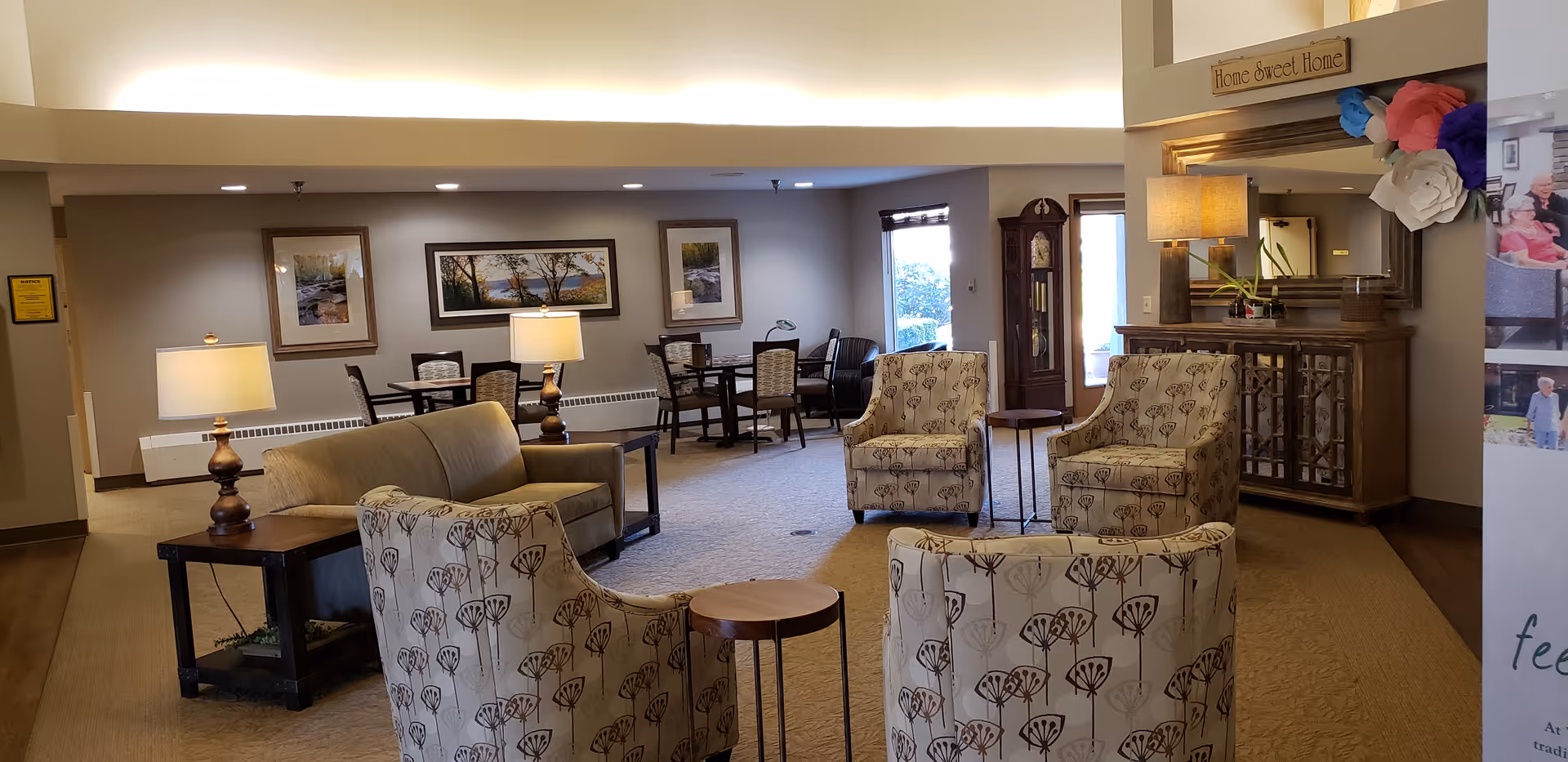 Communal lounge area with a sofa, patterned armchairs, side tables and lamps, plus dining tables in the background.