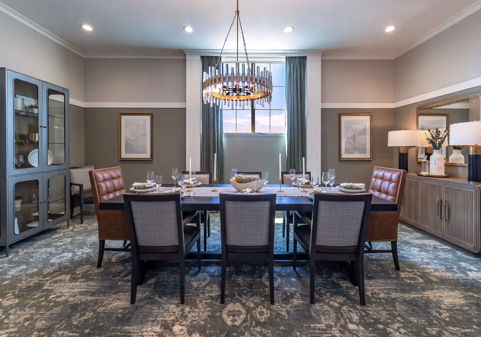 Elegantly furnished dining room with a long table set for eight, a chandelier, sideboard, and display cabinet.