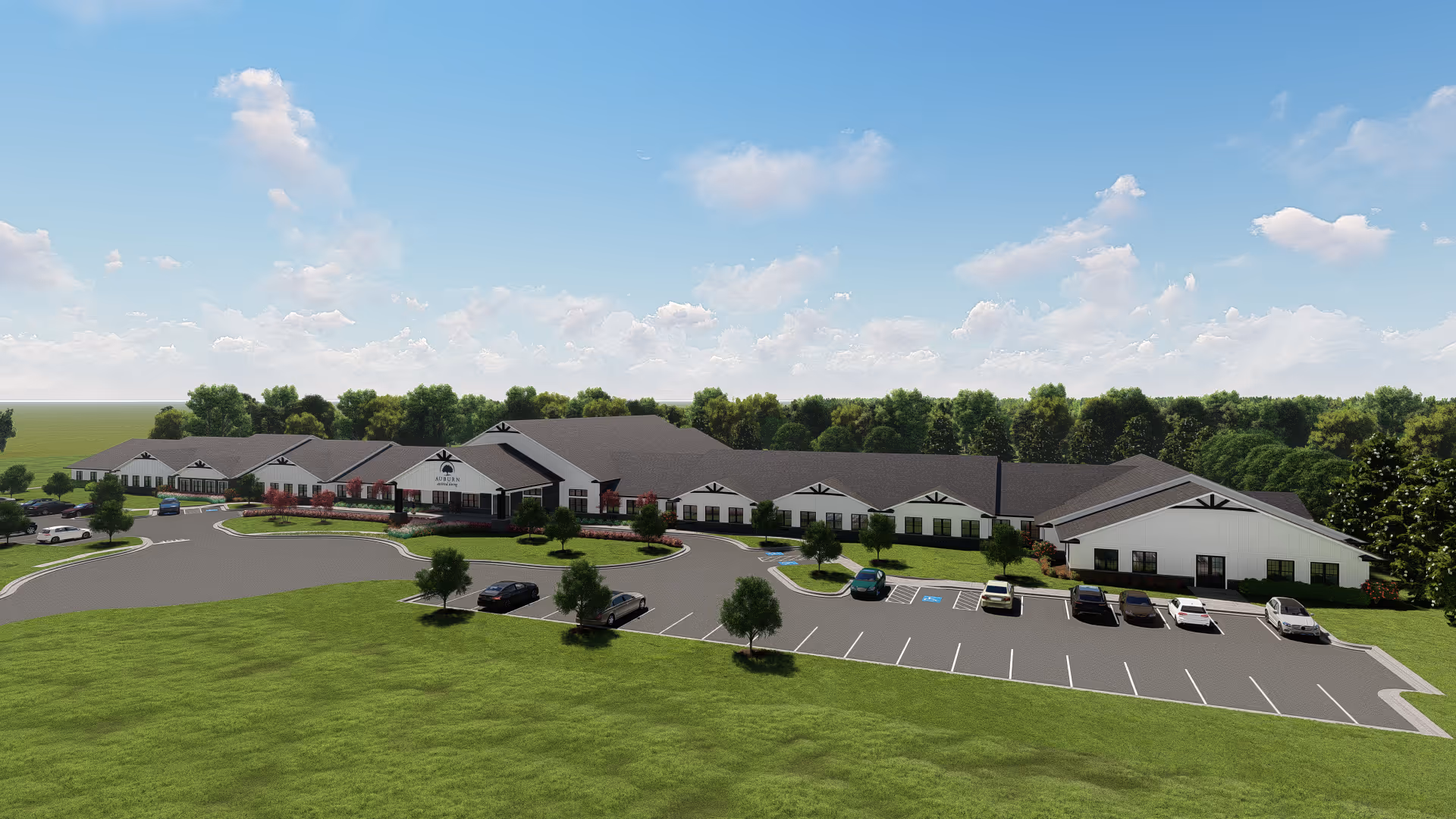 Wide exterior view of a single-story assisted living building with a parking lot, landscaped lawns and trees under a blue sky.