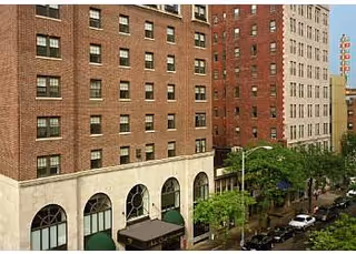 A multi-story brick building with arched storefronts and green awnings along a tree-lined street.