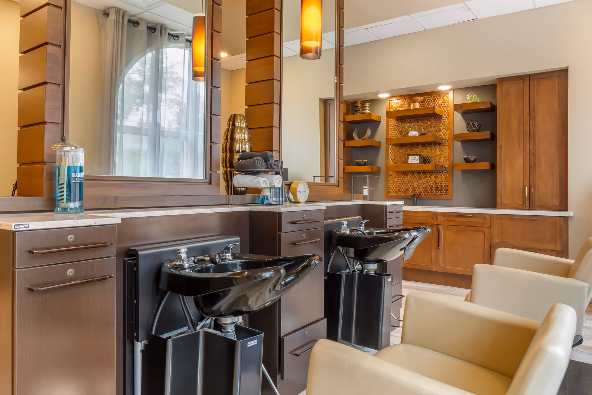 Salon-style interior showing two black shampoo sinks, beige chairs, large mirrors, and wooden cabinetry and shelving.