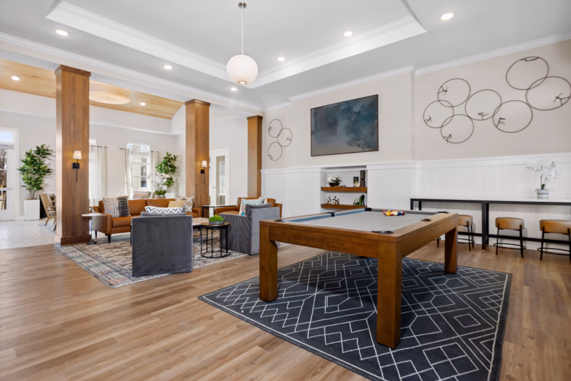Spacious senior living common room with a pool table on a rug, seating areas, wooden columns, and wall decor.