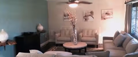 Facility living room with beige sofas, teal accent wall, glass vase centerpiece, and artwork.