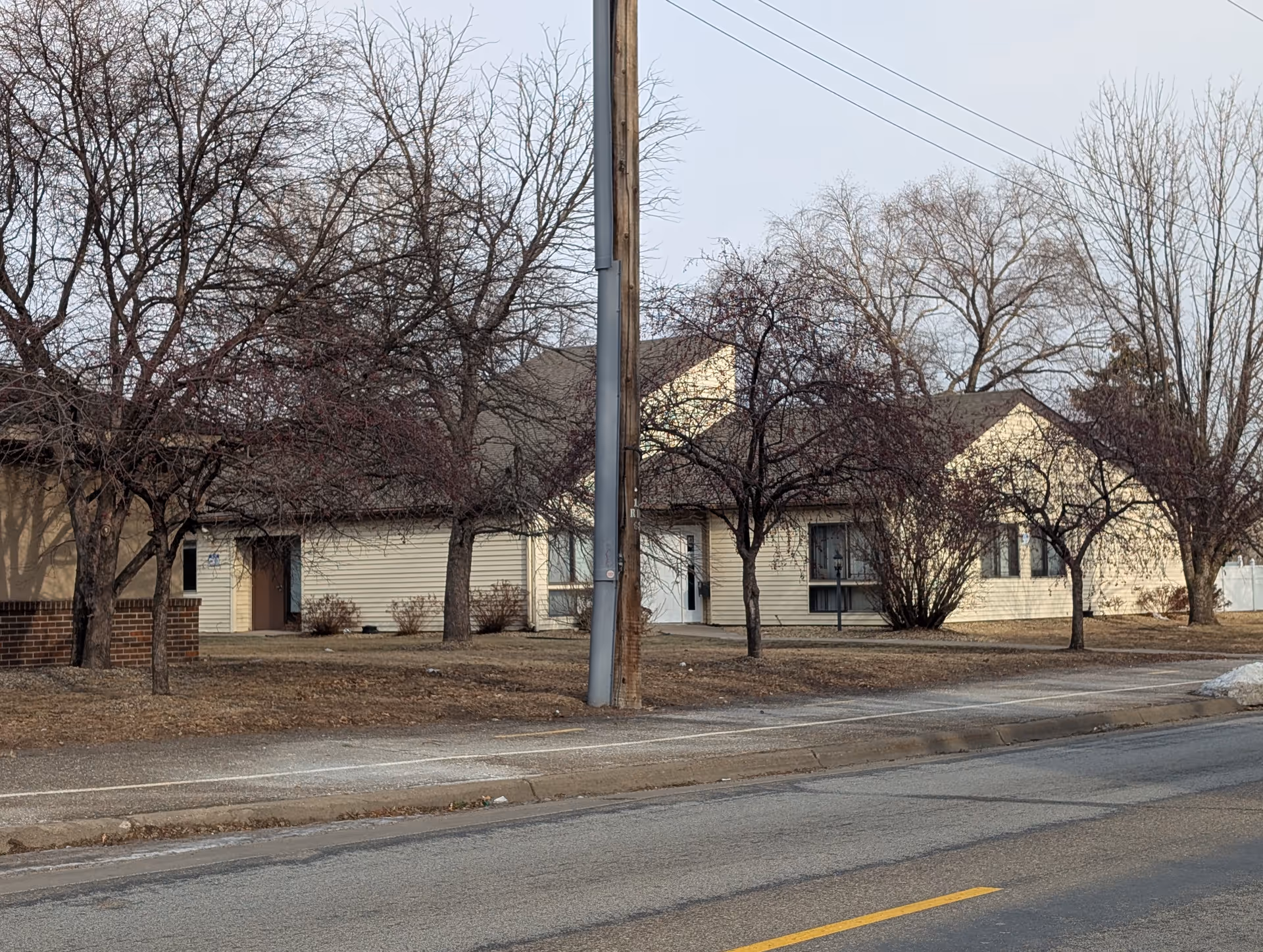 Street view of a beige single-story rehabilitation building with leafless trees, a utility pole, and a sidewalk.