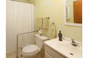 Small accessible bathroom with a toilet, sink and mirror, shower with curtain, grab bar, and towels on a rack.