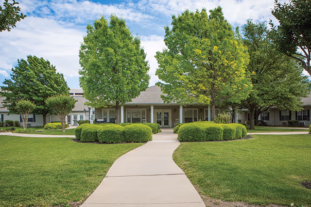 Front view of Brookdale Collin Oaks facility with walkway, trees, and manicured lawn.