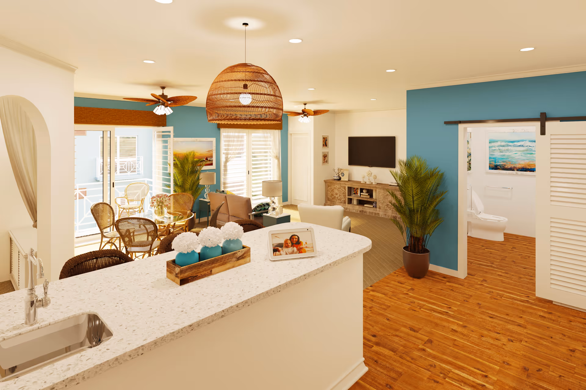 A bright and airy senior living space featuring a kitchen island with a sink and decorative flowers, a cozy living room with a TV mounted on the wall, a dining area with wicker chairs and a glass table, ceiling fans, and a bathroom visible through a sliding barn door. The walls are painted in a combination of white and teal, and the floor is wooden.