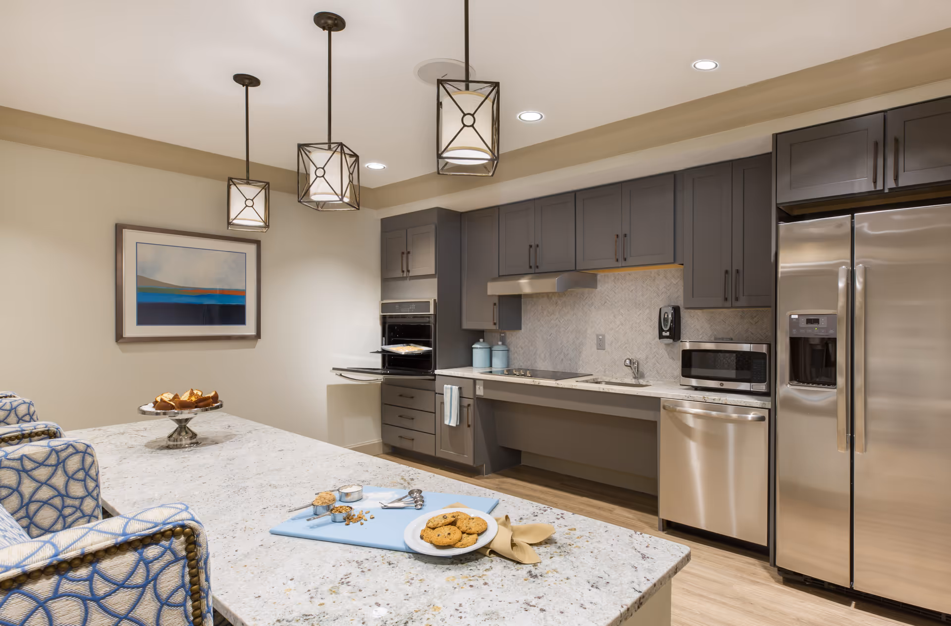 Modern kitchen with a large island, pendant lights, gray cabinets and stainless steel appliances.