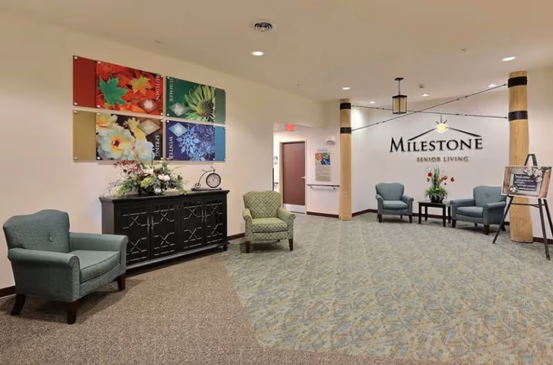 Reception lobby of Milestone Senior Living with armchairs, decorative wall art, and the facility logo on the far wall.