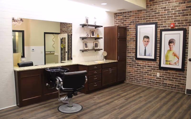 Interior view of a hair salon featuring a granite countertop, a black salon chair, and framed portraits on the brick wall.