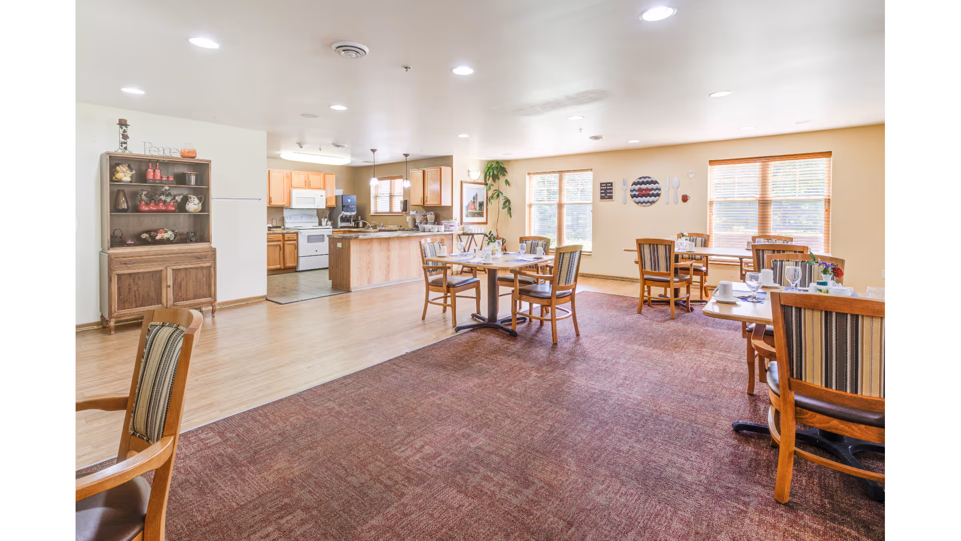 Spacious dining room with wooden tables and chairs and an open kitchen area in the background.