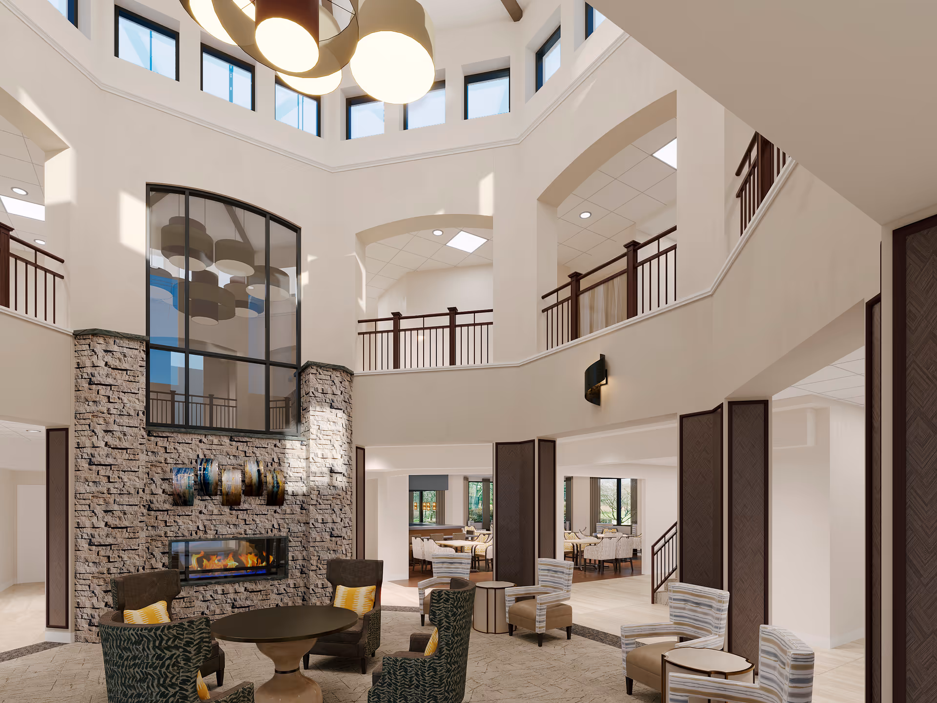 Spacious and well-lit senior living facility common area with high ceilings and large windows near the ceiling. The room features a stone fireplace with a modern fire, surrounded by comfortable armchairs and small tables. There is a second-floor balcony with railings overlooking the area, and a dining area with tables and chairs is visible in the background.