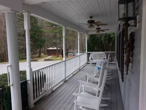 Long covered porch with white rocking chairs and ceiling fans along railing.
