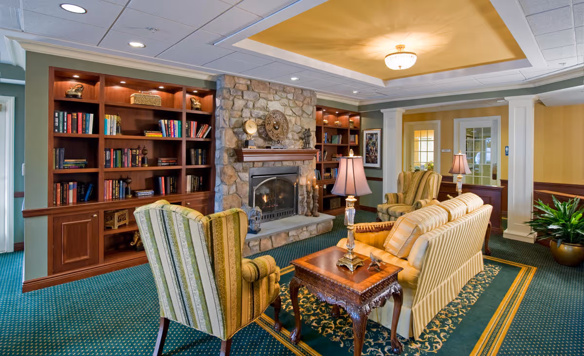 Comfortable lounge area with striped armchairs and a sofa arranged around a stone fireplace, flanked by built-in bookshelves and lamps.