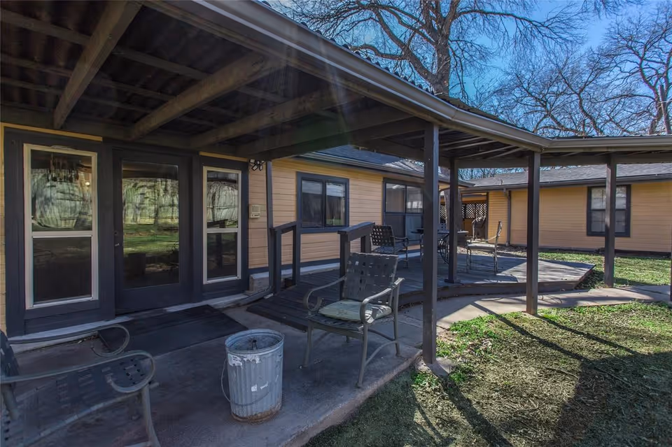 Covered outdoor patio with metal chairs and tables in front of a single-story yellow building.
