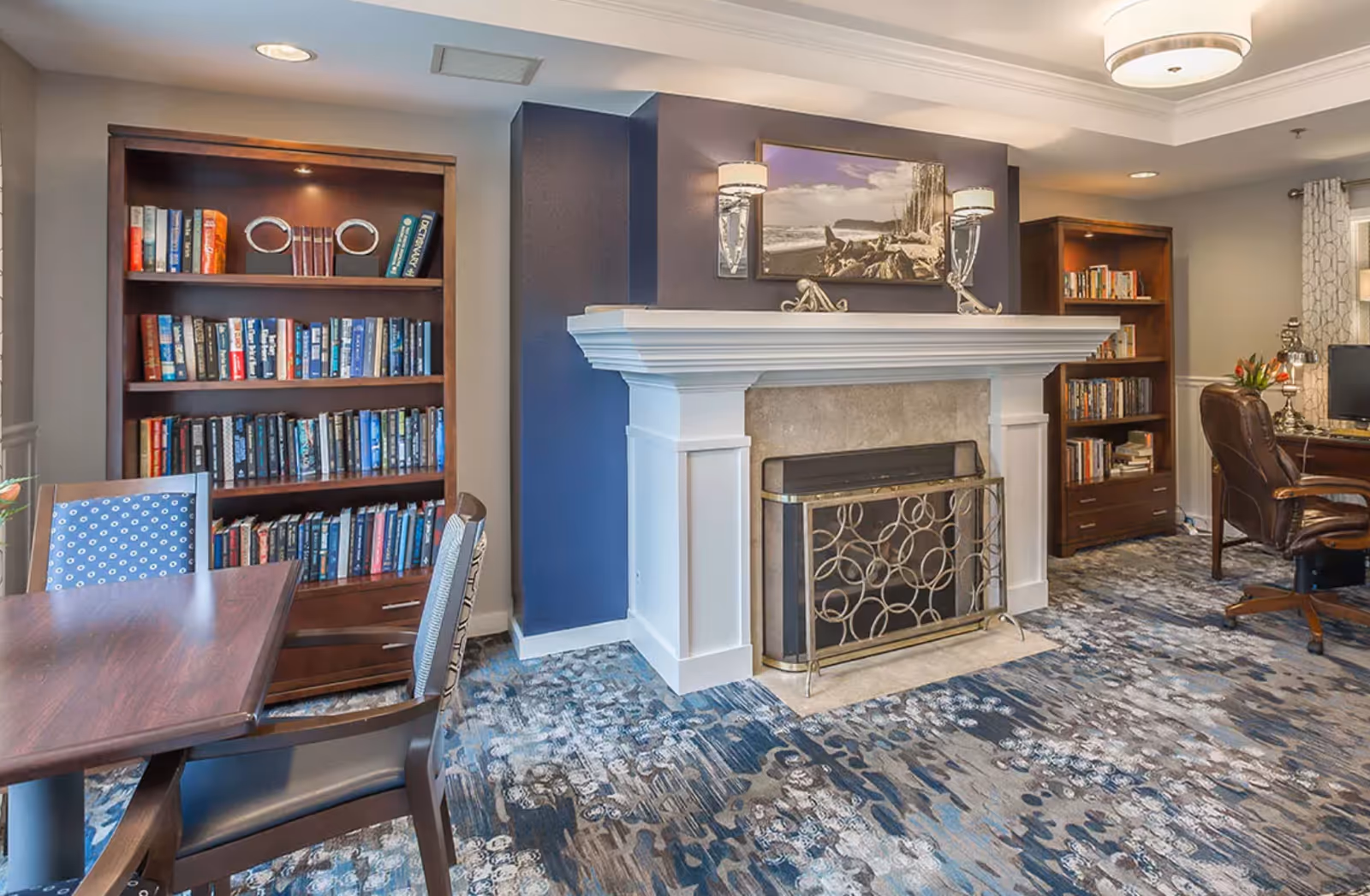 Cozy common room with a fireplace flanked by bookshelves, seating, and a table.
