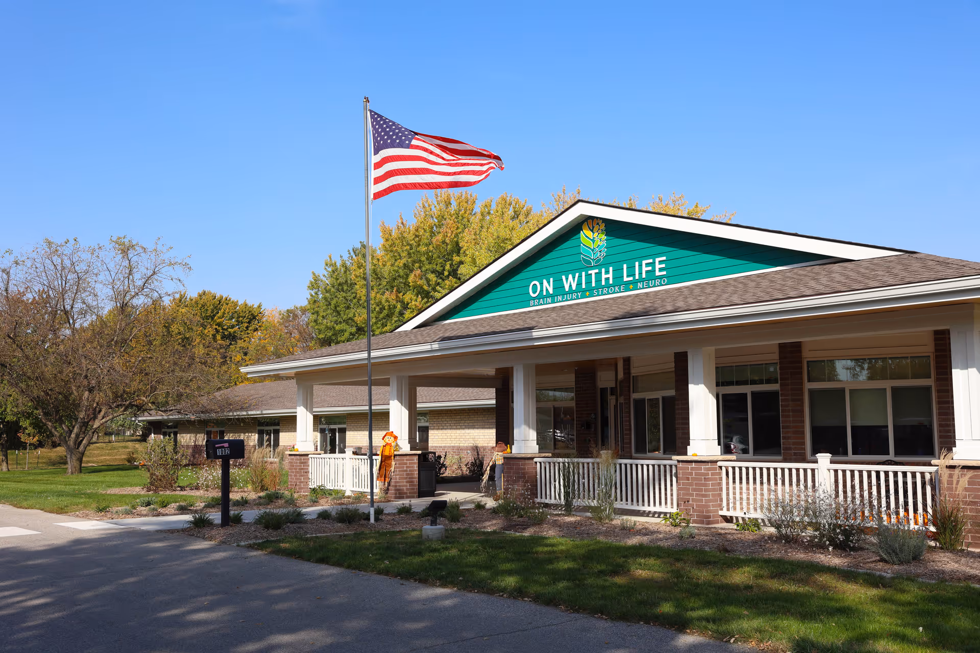 Exterior front entrance of the 'On With Life' long-term care facility with a porch and an American flag flying in front.