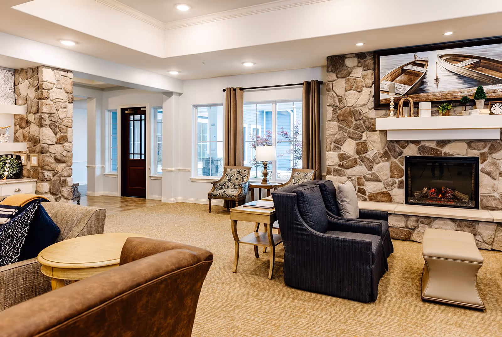 Cozy senior living lounge with a stone fireplace, armchairs, sofas, side tables and wall art.