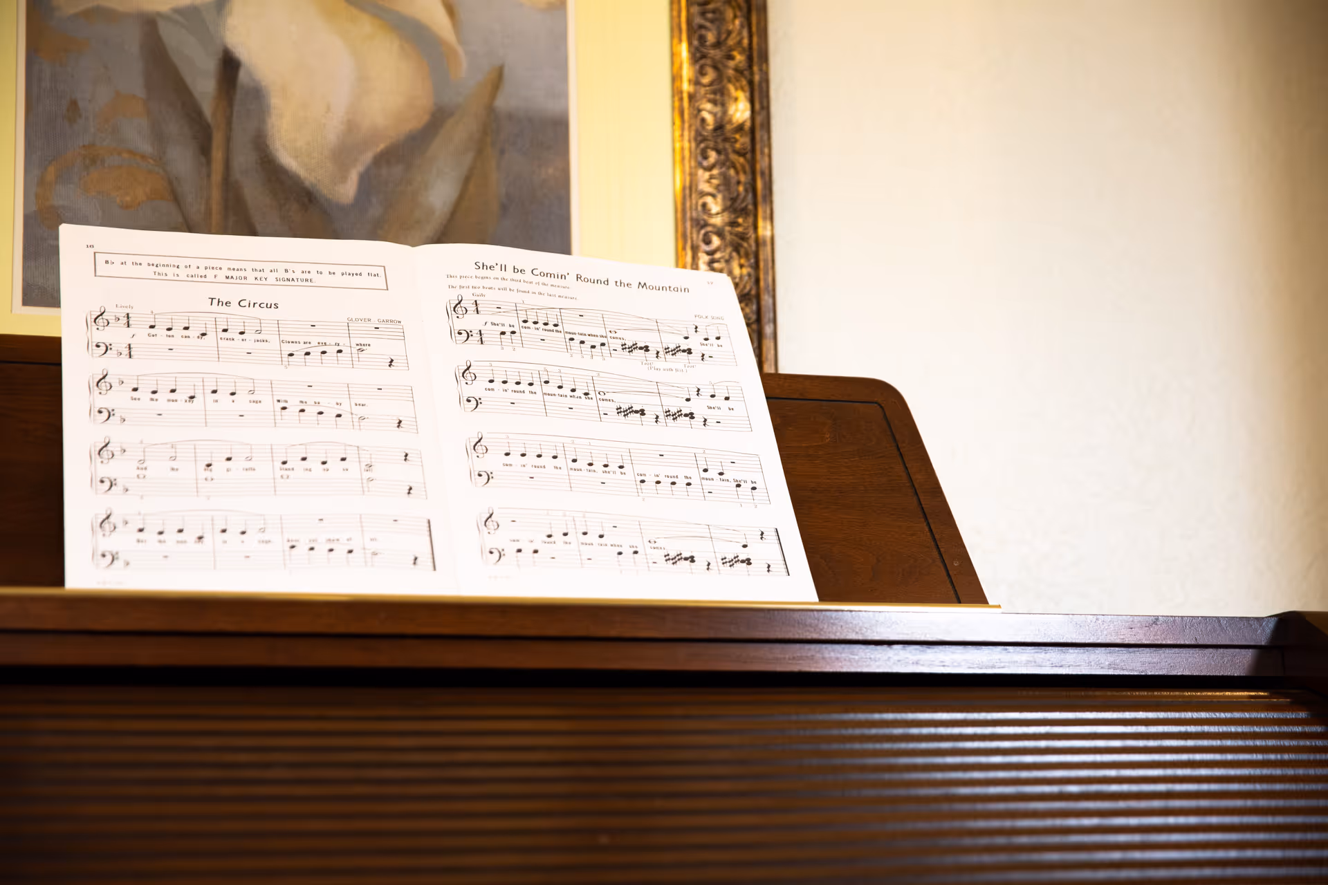 Sheet music on a wooden piano stand with a framed painting on the wall behind it.