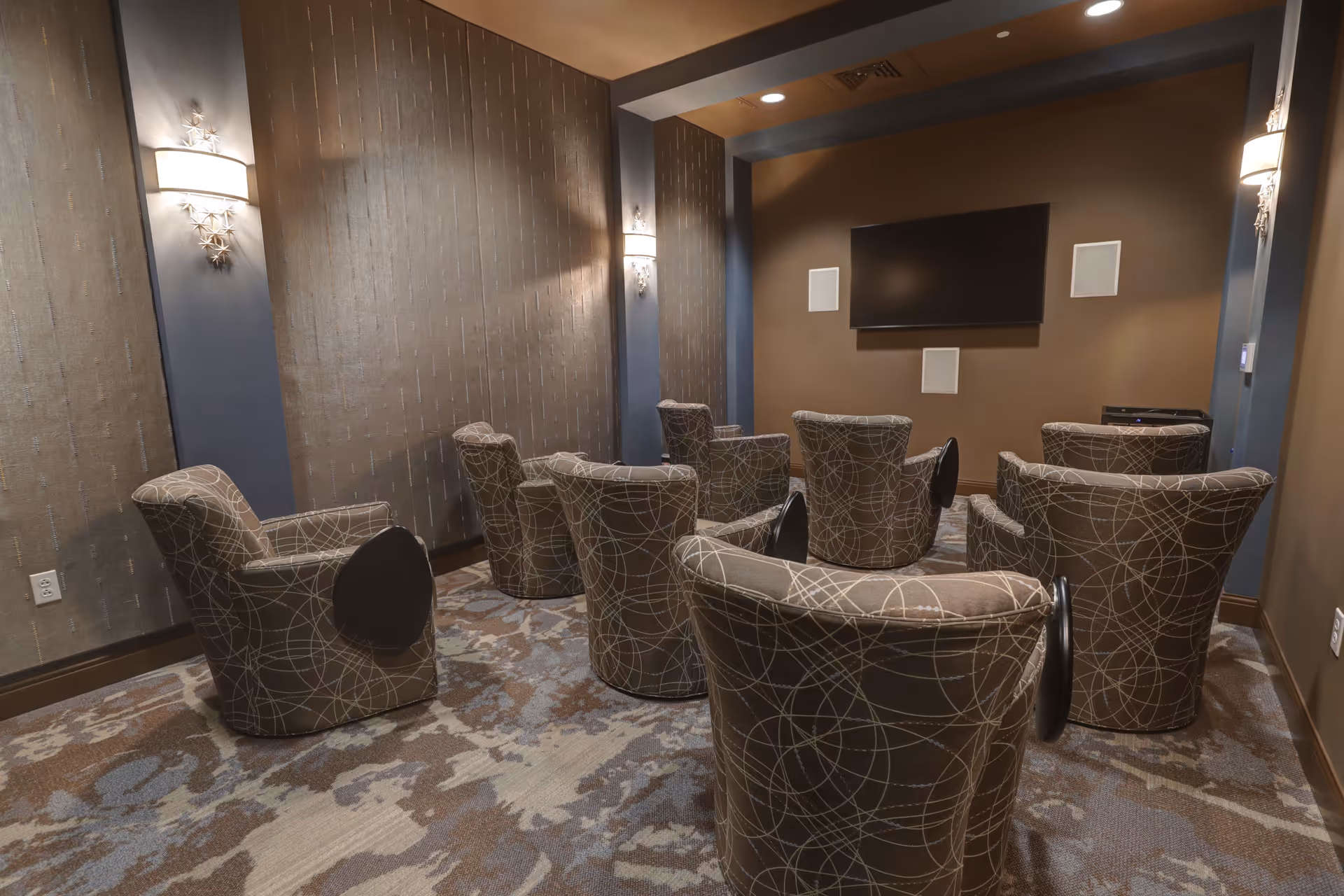 Small media room with several patterned armchairs arranged facing a wall-mounted flat-screen TV.