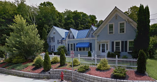 Exterior view of Westboro House, a light-blue senior living building with white trim and blue awning.