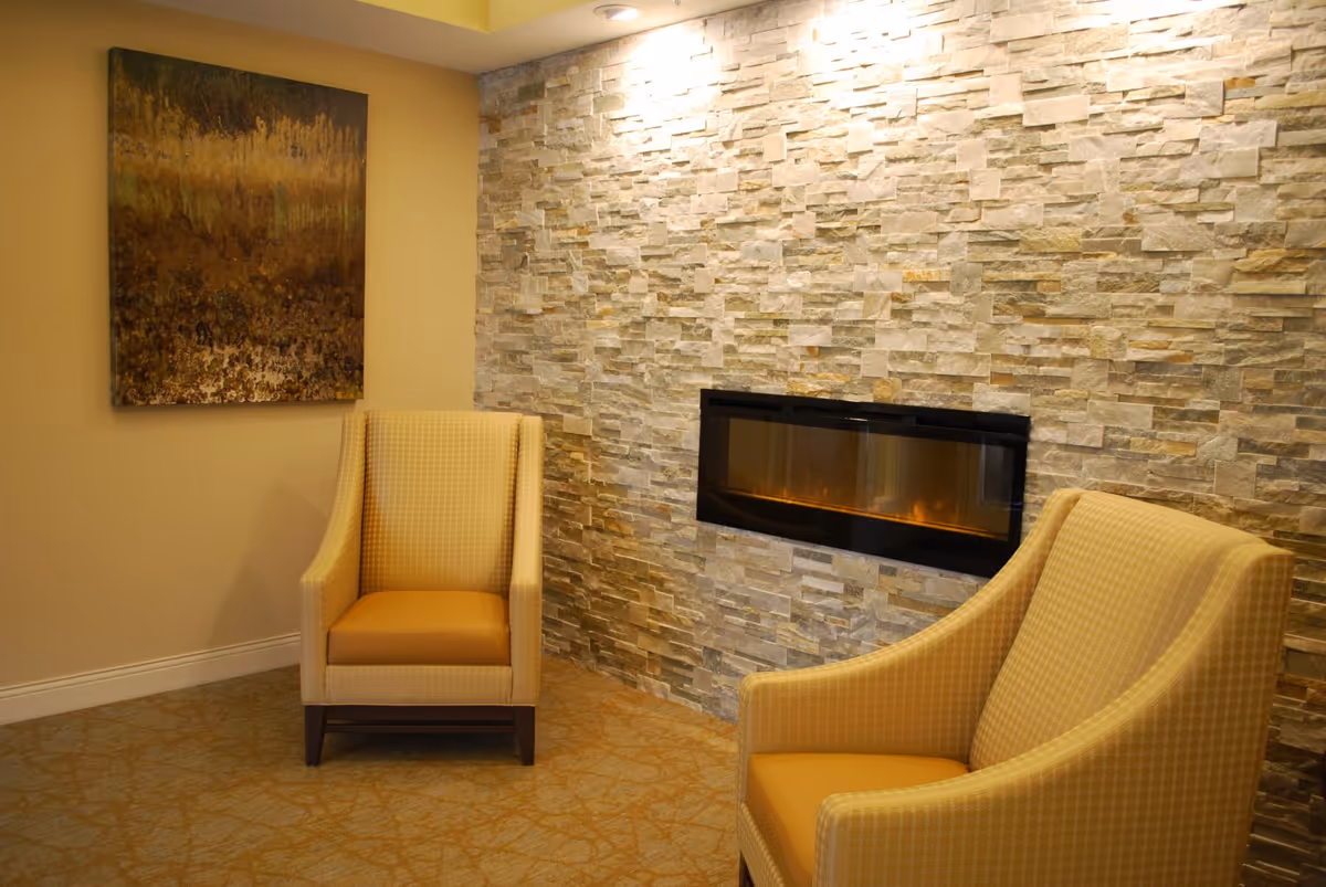 Two upholstered armchairs sit in a cozy seating area beside a wall-mounted fireplace set into a stacked stone accent wall.