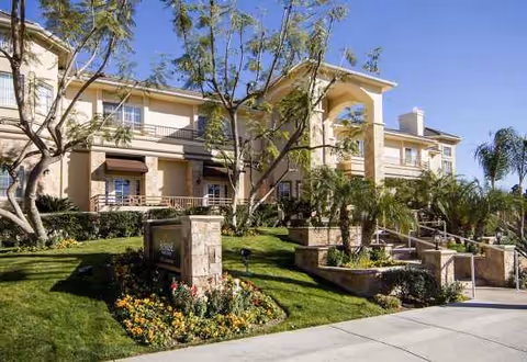 Two-story Sunrise of Yorba Linda senior living building with landscaped lawn, trees, and entry stairs.