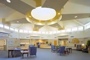 Bright, spacious senior living lounge with blue chairs and a circular ceiling light.