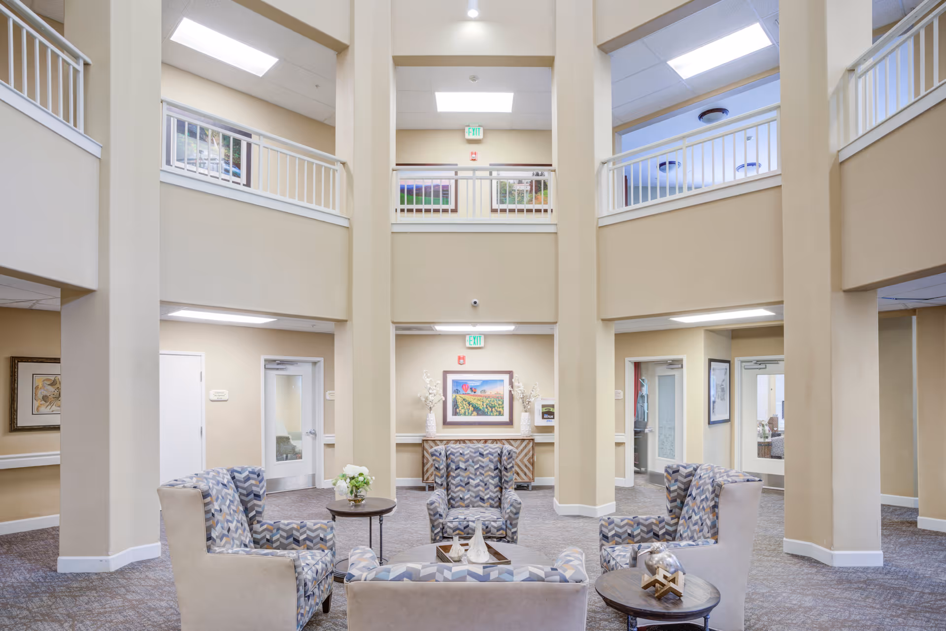 Two-story atrium lobby with a circular seating area of patterned armchairs, side tables, and artwork.