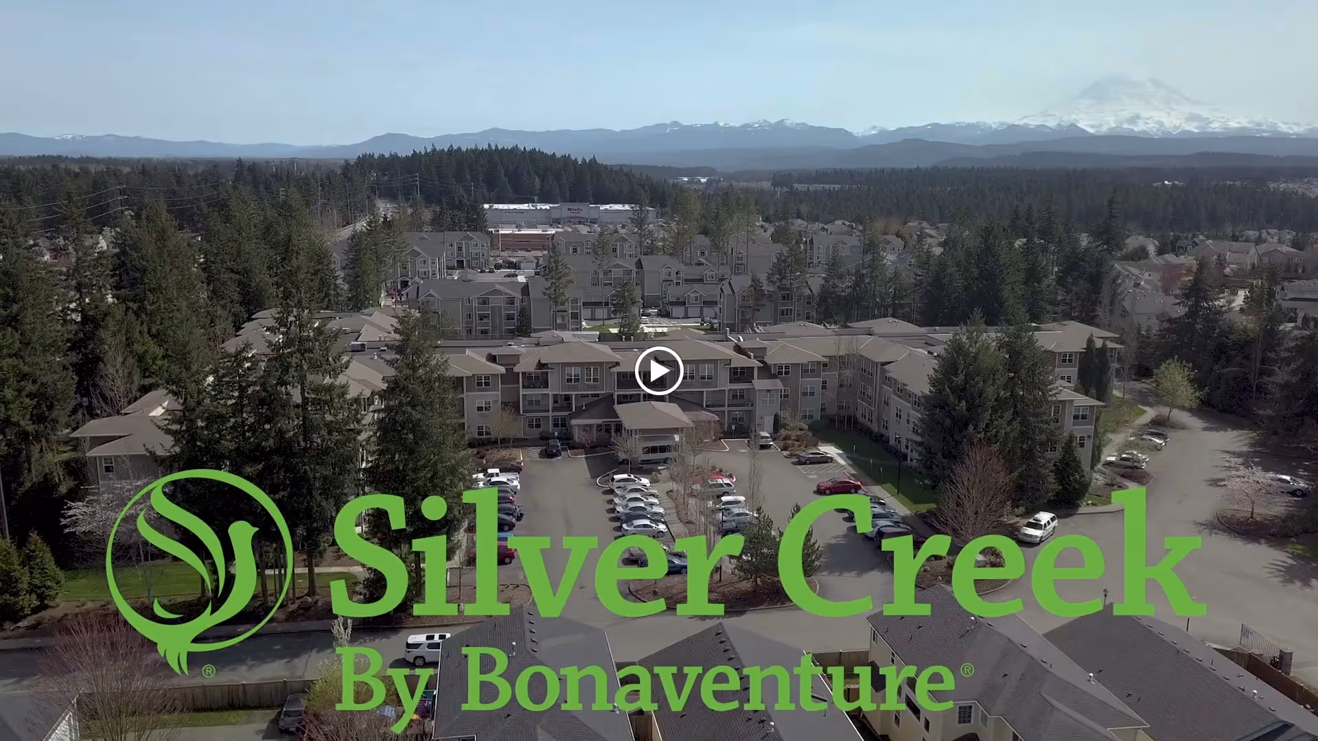 Aerial view of the Silver Creek by Bonaventure senior living campus with parking lot, trees, and distant mountains.