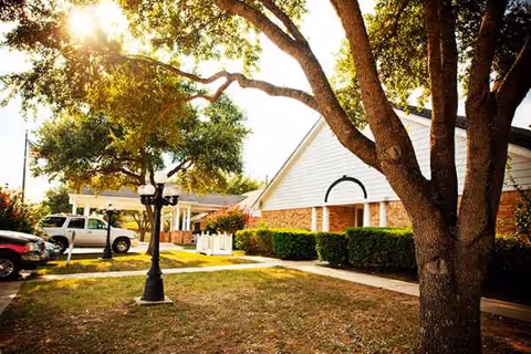 Exterior view of Focused Care at Brenham, showing front entrance, trees, and parked cars.