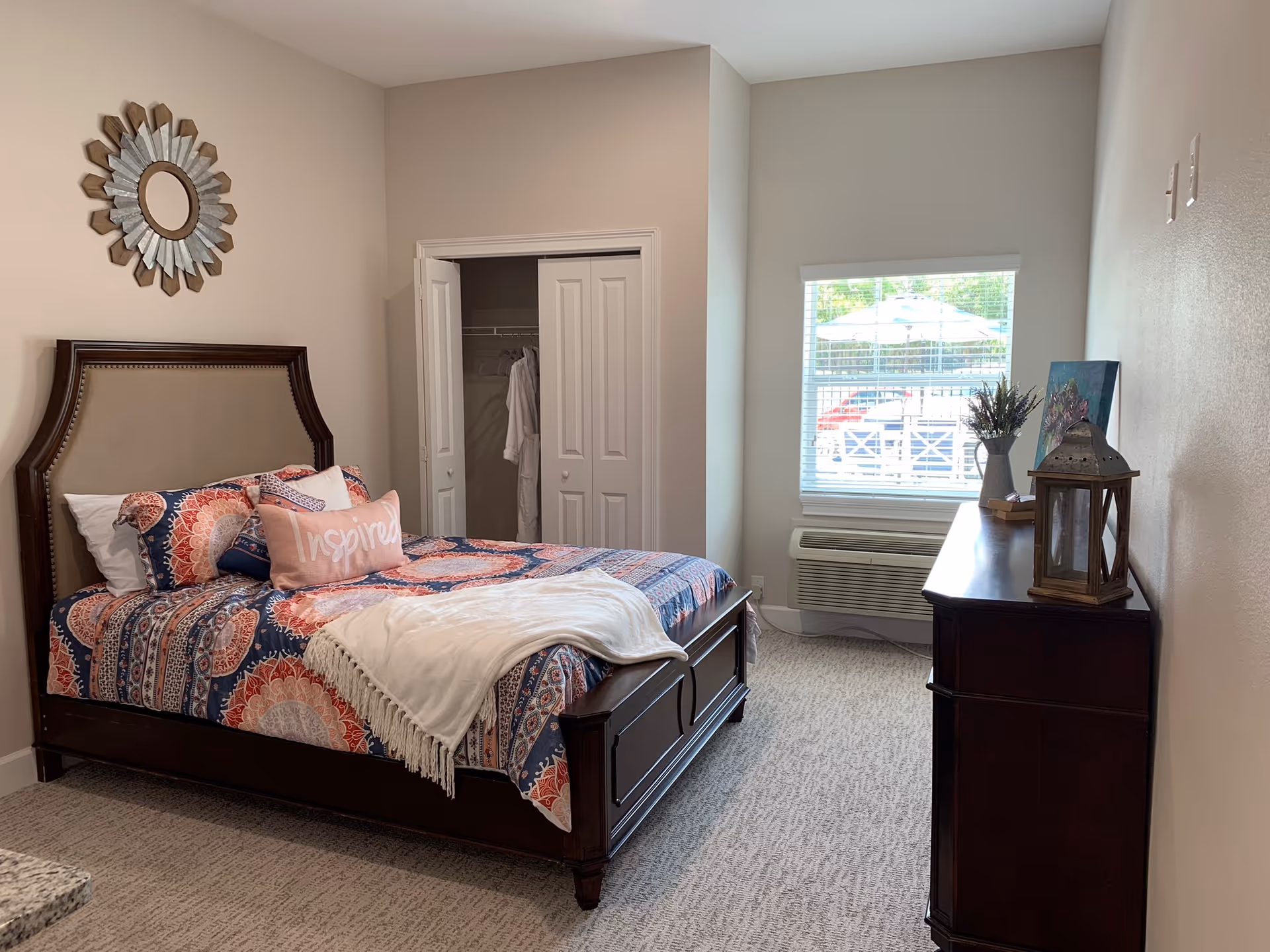 Well-decorated bedroom with a bed dressed in patterned bedding, a dresser, window, and an open closet.