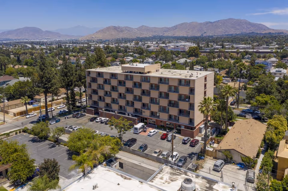 Aerial view of a multi-story care building with a parking lot, surrounding trees, and distant hills.