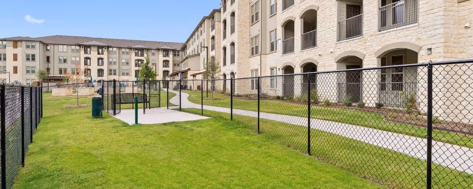 Exterior courtyard of a multi-story senior living building with a fenced grassy area, walkways, and balconies.