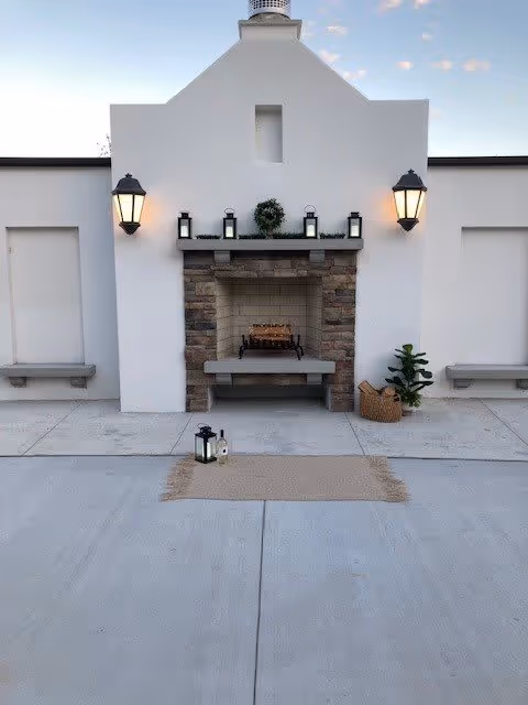 Courtyard with a white stucco wall and built-in stone fireplace, flanked by wall lanterns, benches, a rug, and decorative lanterns.