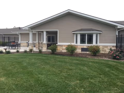 Single-story building front with a covered patio, bay window, stone trim, and a neatly mowed lawn.