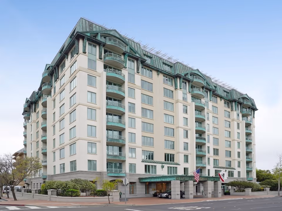 Exterior view of a multi-story senior living facility named The Stratford, featuring balconies, large windows, and a covered entrance with American and California state flags.