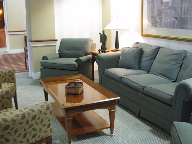 A lounge area with green upholstered sofa and matching armchairs around a wooden coffee table and a lamp on a side table.
