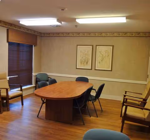 A wooden oval table with chairs in a softly lit senior living dining area.