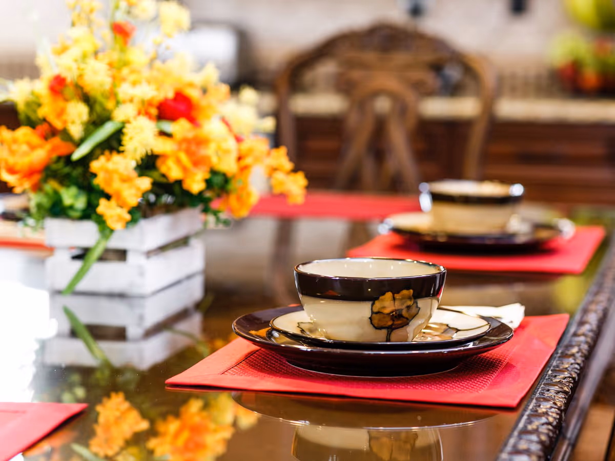 Close-up of a dining table set with decorative plates and bowls on red placemats, with a centerpiece of vibrant yellow and orange flowers in a white wooden box.