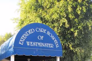 Blue awning with white text that reads 'Extended Care Hospital of Westminster' in front of a large green tree.